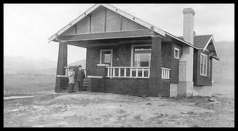 Ted, Helen and Eve (baby) Dewdney standing in front of their house