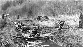 Soldiers crawling through a trench filled with mud and water at the Canadian Battle Drill School near Coldstream Ranch