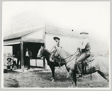 Two men on horse back next to small grocery store