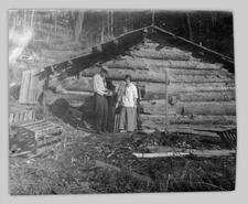 Dr. Craig McCullough & Mrs. McCullough in front of log cabin