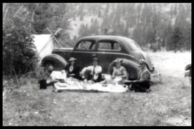 Group having camping lunch beside automobile