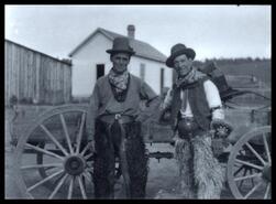 Two cowboys wearing hairy chaps and standing in front of buckboard