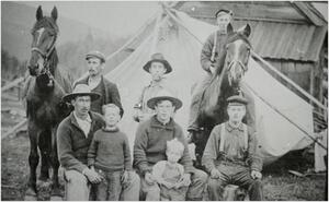 Group portrait of men with young boys in front of a tent with two horses