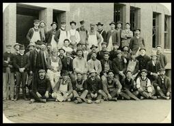 Group of construction workers posing in front of either the Courthouse or Post Office in Grand Forks, B.C.