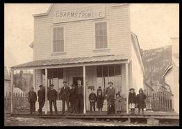 Teacher Hartley Schuyler standing with children on porch of G.B. Armstrong Store in Lower Nicola
