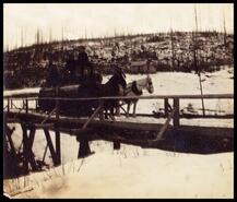 Horse team pulling a sled with logs over a bridge in winter