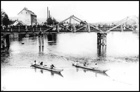 Shuswap Indigenous women in two dugout canoes racing on the Shuswap River under the Enderby bridge