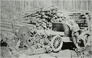 John Cullis posed next to his car with his saw and wood pile