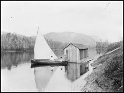 Two women and a man in a sailboat beside a boathouse on the Shuswap River