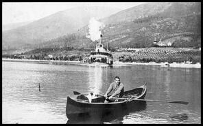 Man in a row boat with the S.S. Moyie and C.P.R. Hotel at Balfour in the background