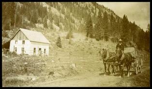 Wagon travels on dirt road past unknown homestead
