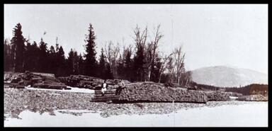 Unidentified man and woman sitting on log pile in Adams River Lumber Company yard