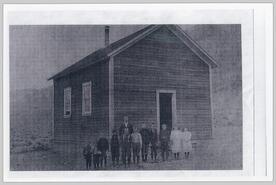 A small group of school children stand outside of a school house