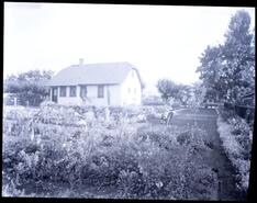 Exterior of unidentified house with three individuals in the garden