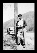 Unidentified boy leaning on telephone pole beside a road