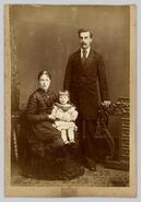 Unidentified man standing, with woman seated and child in lap