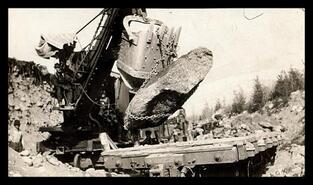 Steam shovel moving large boulder as part of K & S Railway line reconstruction