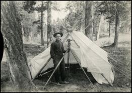 Percy Lake with surveying instrument in front of a tent at Banff-Windermere Highway survey crew camp
