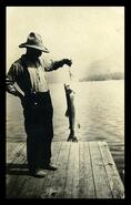Ole Johnson standing on a wharf with a nice trout probably at Christina Lake