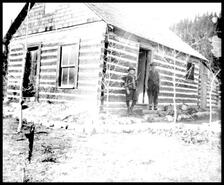 Two men standing on front steps of log cabin