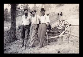 Three men standing in front of wooden wagon