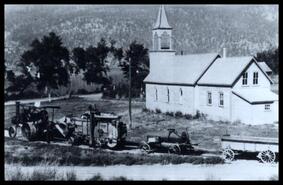 Guichon steam tractor pulling threshing equipment past Our Lady of Lourdes church at Nicola Lake